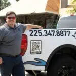 Smiling businessman in gray polo shirt standing next to white work truck with phone number