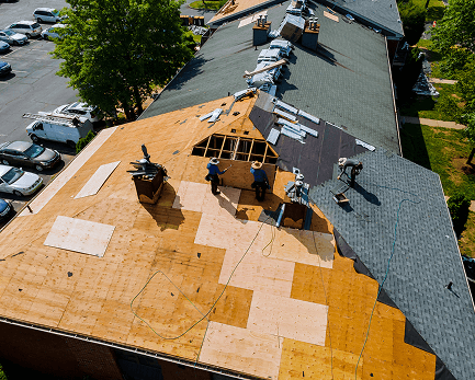 Roofing professionals work on repairing a large roof with plywood.